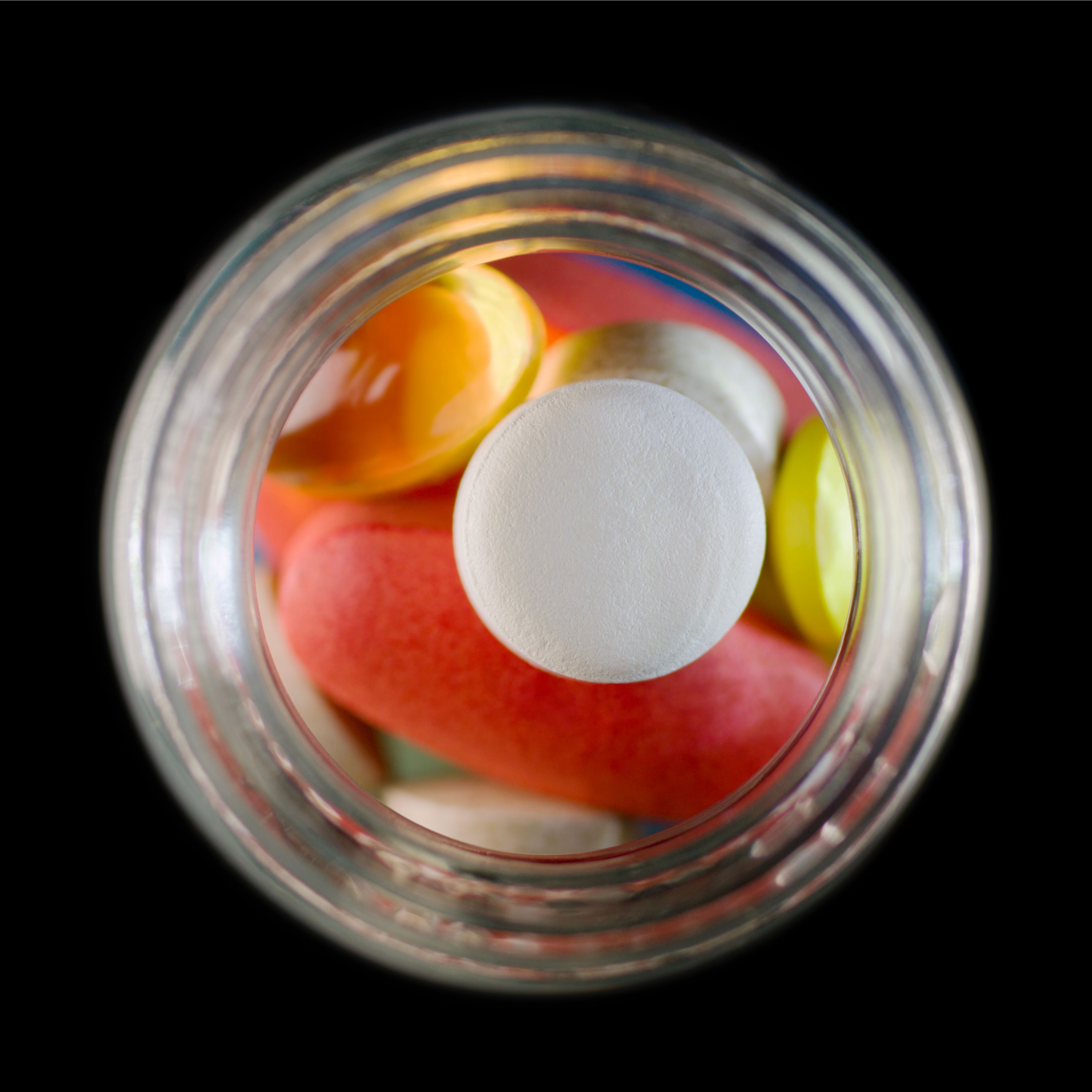 Colorful assortment of pills viewed from the top of an open glass jar.