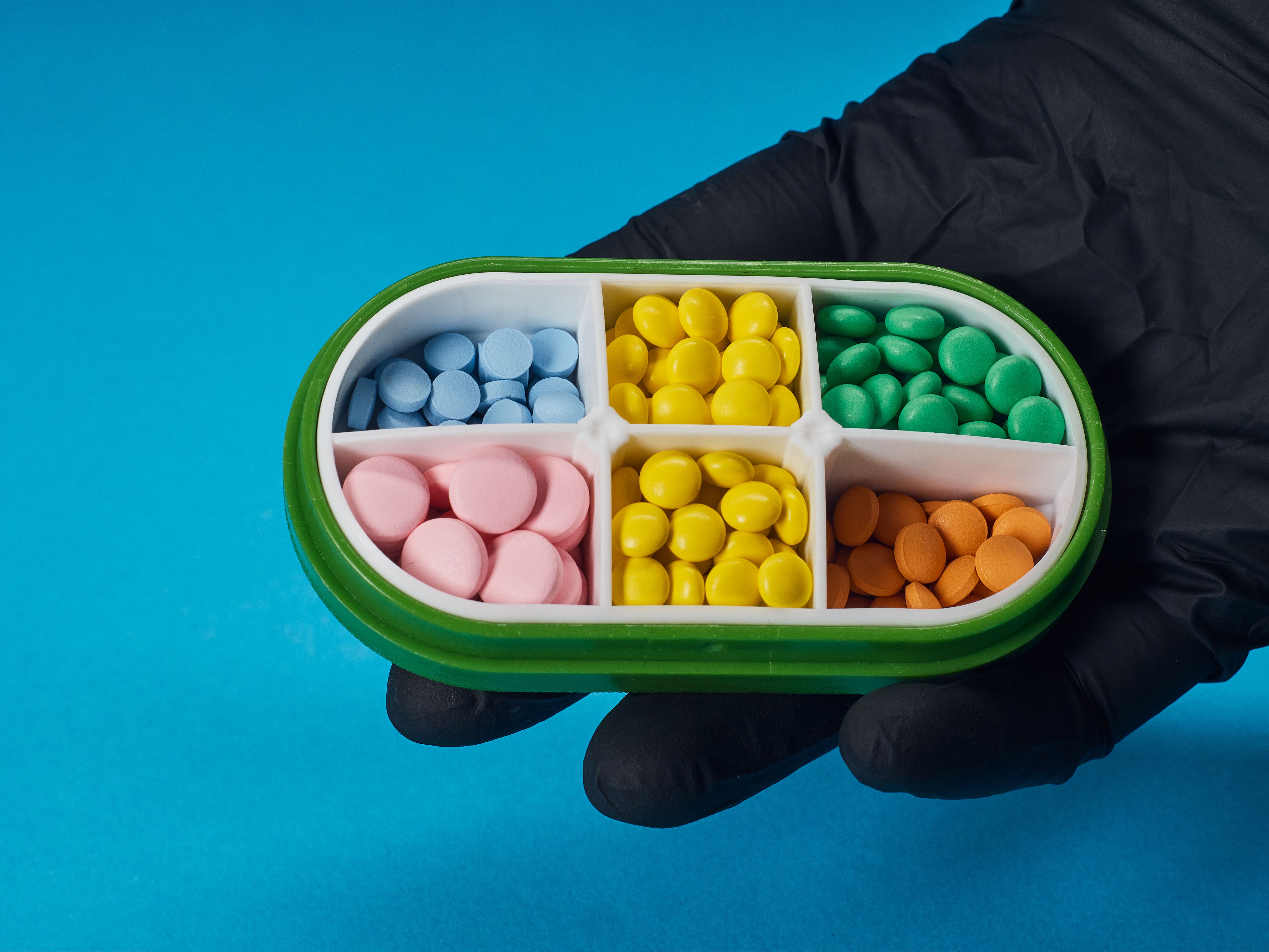 Colorful pills in a four-compartment box held by a gloved hand on a blue background.