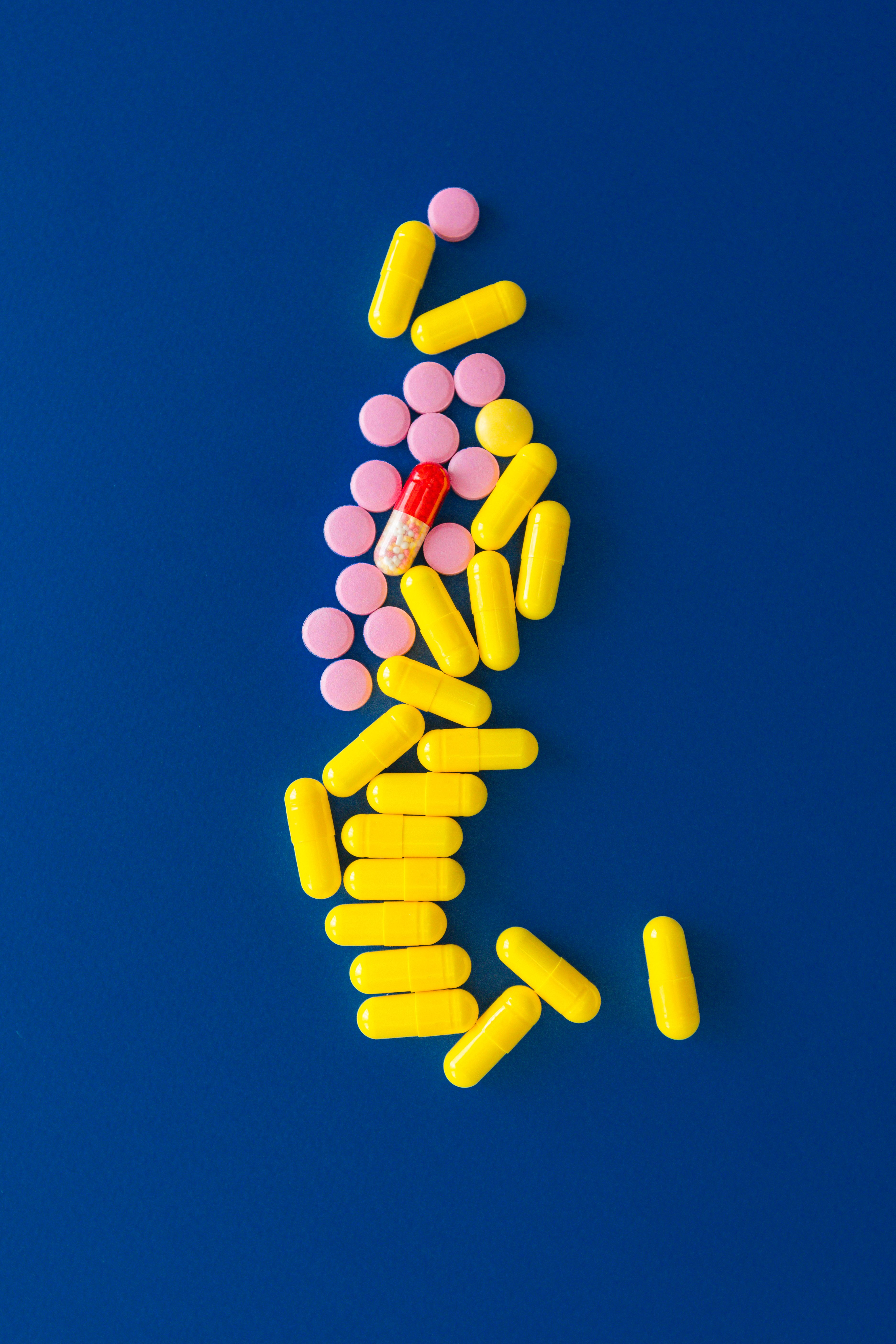 Yellow and pink pills creatively arranged on a blue surface. Tablets of various colors.